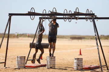 pair of muddy athletes passing a ring obstacle