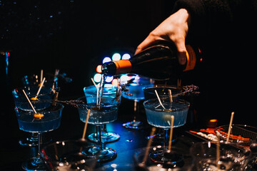 Bartender pouring cocktails over ice at a dimly lit bar. Nightlife, cocktail preparation, mixology, party atmosphere, bar scene.