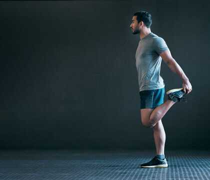 Stretching legs, fitness and man in gym for exercise, training and warm up for runner workout on gray background. Health, sports and person with mockup space for wellness, performance and flexibility