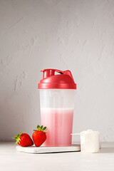 Pink strawberry protein drink shake in a shaker bottle and protein powder in a scoop. Food supplement.