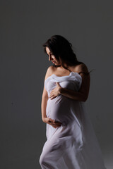 Fototapeta premium Beautiful pregnant woman in white flying cloth. Big pregnant belly. Pretty woman waiting child. Brunette. Studio light