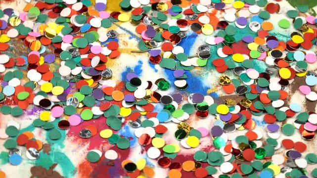Multicolored confetti scattered randomly on white patterned fabric, festive background