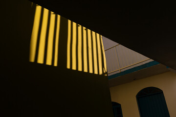 Sunlight casts dramatic shadows on a yellow wall, creating a striking geometric pattern
