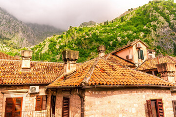 landscape of beautiful vintage houses with orange tile roofs in vintage venetian style to amazing high green mountain with ancient buildings on slopes and nice cloudy sky on background