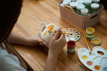 Top view of woman painting with brush on clay pottery mug in workshop