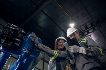 Engineer with helmet safety standing by robotic arm and operating machine in industry factory, technician worker check for repair maintenance electronic operation