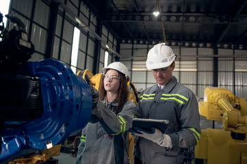 Engineer with helmet safety standing by robotic arm and operating machine in industry factory, technician worker check for repair maintenance electronic operation