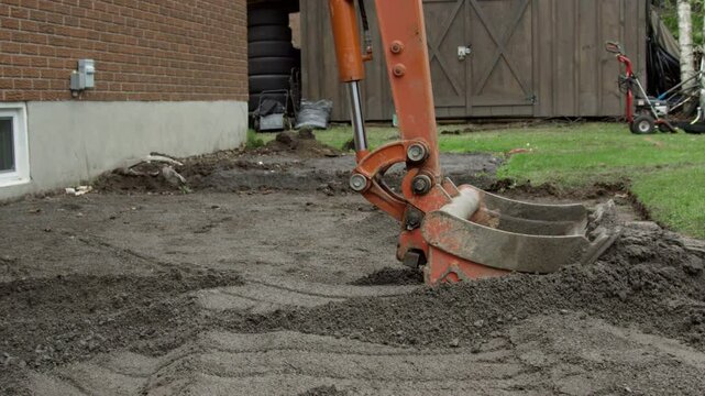 Mini excavator begins digging out foundation for repairs on residential house - side profile of excavtor bucket