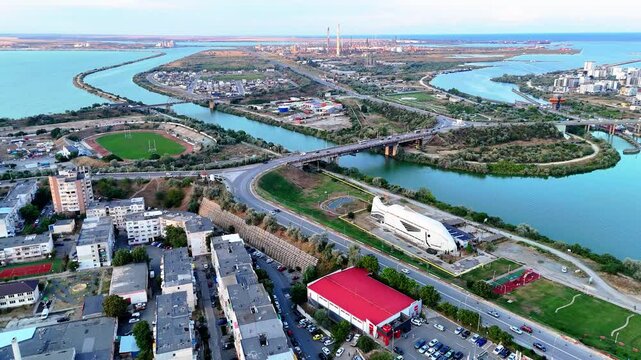 Reverse aerial view of a fish like structure and a industrial area behind it near Navodari