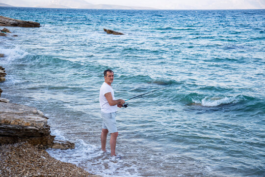 fisherman by the ocean with fishing rod looking at camera