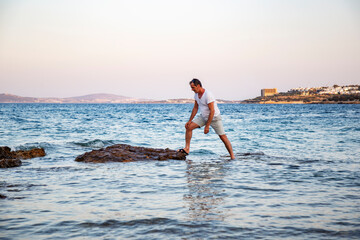 Man exploring coastal rocks in the sea, steps over rocks