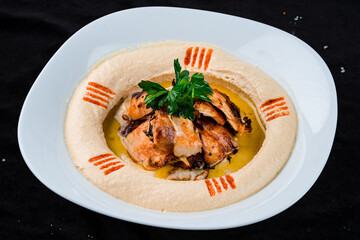 Fresh chickpea hummus with fried chicken fillet, parsley and oil in a plate.
