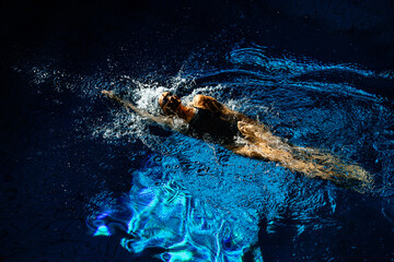 Female athlete swims with a back stroke. Splashes of water scatter in different directions