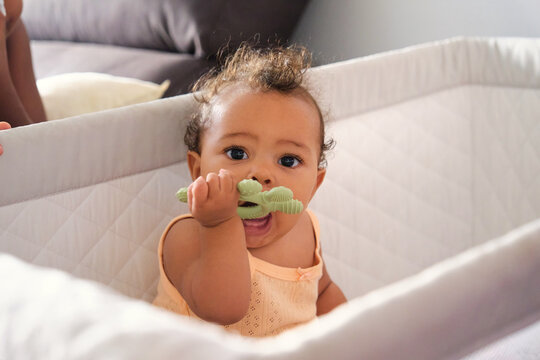 Adorable baby girl chewing on teething toy in crib