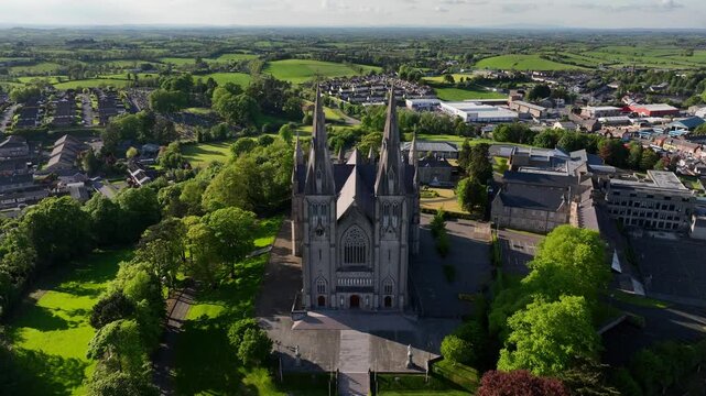 St. Patrick's Cathedral, County Armagh, Northern Ireland, May 2023. Drone pushes forward descending towards the Roman Catholic architecture pushing between the Gothic Revival spires on a sunny day.