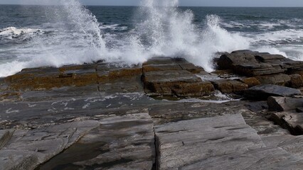 Ocean waves and surf breaking on peaceful rocky coastline  beach as sunshine reflects on water during summertime along seashore in Maine