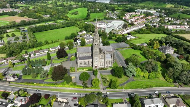 St. Macartan's Cathedral, County Monaghan, Ireland, September 2022. Drone orbits clockwise in a wide high angle view of the architecture by busy road surrounded by trees outside Monaghan town.