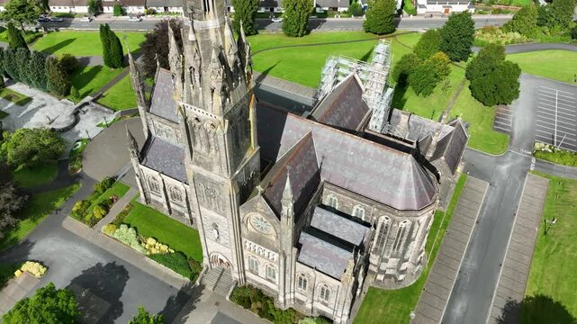 St. Macartan's Cathedral, County Monaghan, Ireland, September 2022. Drone pulls backward showcasing the Roman Catholic architecture surrounded by trees gardens and buildings on a bright sunny day.