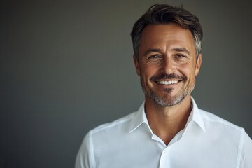 Obraz premium Smiling businessman in a crisp white shirt, looking directly at the camera, against a neutral background with generous copy space