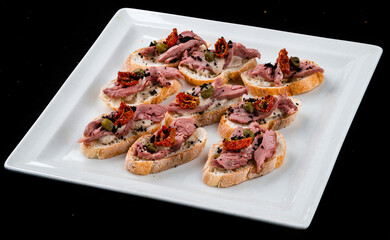 Bruschetta with meat, tomatoes, capers and sauce in a white plate.