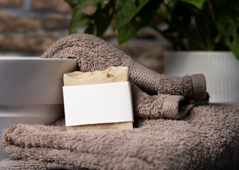 Soap bar with blank label on brown folded towels near plant and basin in bathroom, mockup