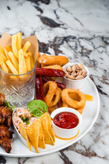 Set of snacks for beer French fries, breaded mozzarella cheese, chicken legs, onion rings coated with breadcrumbs, sausages, nuts and sauces.