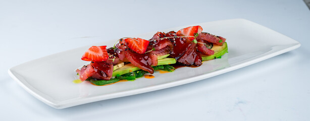 Cold appetizer with tuna, avocado, algae, strawberries, spinach, sesame seeds and sauce.