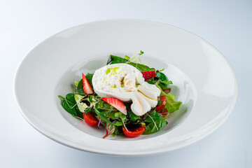 Green salad with burata cheese, strawberries, cherry tomatoes, spinach, beet leaves, lettuce and balsamic sauce in a plate.