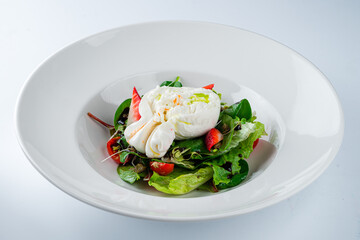 Green salad with burata cheese, strawberries, cherry tomatoes, spinach, beet leaves, lettuce and balsamic sauce on a white background.
