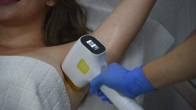 laser epilation, hair removal procedure, young beautiful caucasian smiling brunette woman lying on couch in beauty salon, armpits epilation, spa and cosmetology concept
