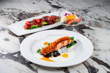 Dinner salmon fillet with spinach and sauces and cold appetizer carpaccio with tuna, avocado, algae, strawberries, spinach, sesame seeds and sauce.
