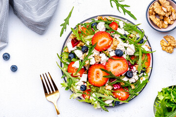Strawberry and feta salad with arugula, lettuce, blueberries, cheese and walnuts, white background, top view