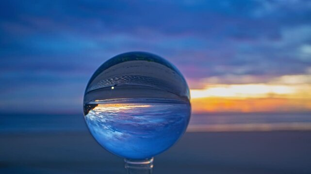 Time lapse A creative capture of a sunset at the beach, viewed through a crystal ball that inverts and magnifies the vibrant colors of the sky and ocean. The blurred background enhances the surreal