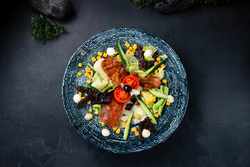 Salad with fried suluguni cheese, sun-dried tomatoes, corn, cucumbers, lettuce and sauce on a dark...