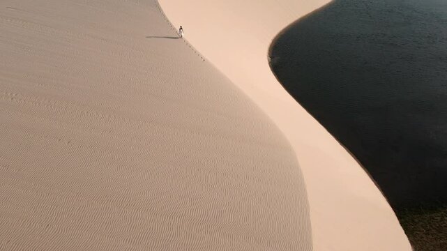 Pessoa andando nas dunas no por do sol com imagem de drone