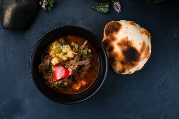 Fresh stewed beef with potatoes, sweet peppers, onions in tomato sauce with herbs and flatbread in a bowl.