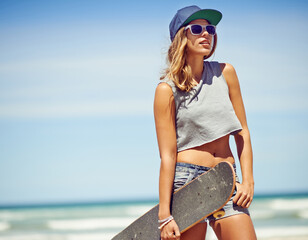 Thinking, travel and woman with skateboard by beach for outdoor activity, sunglasses and vacation with edgy outfit. Girl, longboard and cool or confident with fashion clothes by ocean in California. © ThurstanBuyout/peopleimages.com