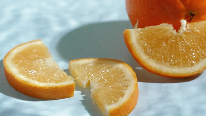 Macro of sliced oranges on a blue textured background with shadow. Close up of orange and sliced citrus with wet blue background and water waving. Natural light. Freshness and citrus concept. Pabulum.