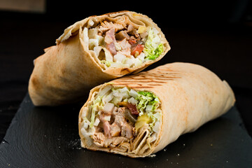 Fresh shawarma from chicken ham, tomatoes, lettuce, herbs, sauce and pita bread on a dark background.