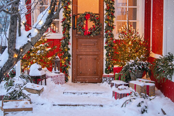 Attractive Christmas entrance decorated with wreath and garlands with snow on the porch.