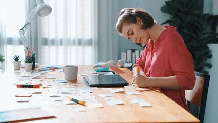 Top view of designer writing idea on colorful sticky notes while sitting at meeting table with tablet display logo design. Professional business woman looking design and making a decision. Symposium.