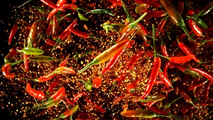 Group of coloured chilli peppers flying on black background.