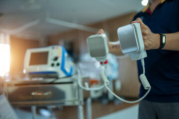 A person is holding a defibrillator in a hospital room