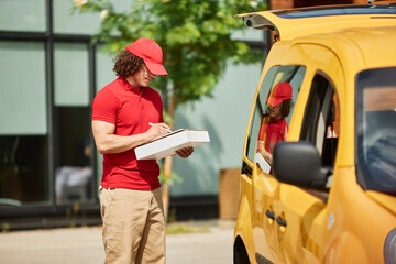 Delivery man in red uniform delivering package while standing next to yellow van in urban area
