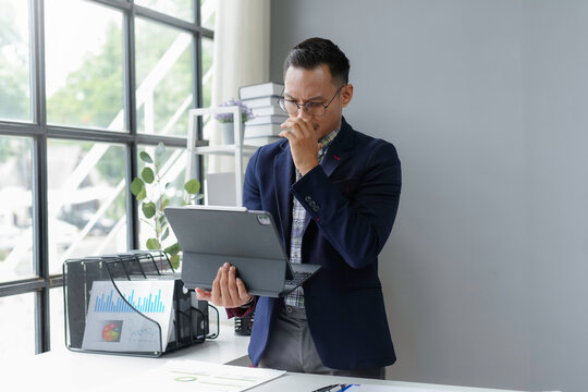 Young businessman feeling stressed and frustrated while working on digital tablet with financial document on table at workplace - Powered by Adobe