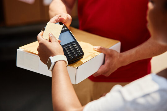Close-up of person's hands conducting credit card payment transaction using card reader with box on counter, wearing white smartwatch on wrist, illustrating modern retail exchange
