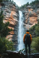 Fototapete Hiker at a majestic waterfall in the mountains on a cloudy day © olegganko