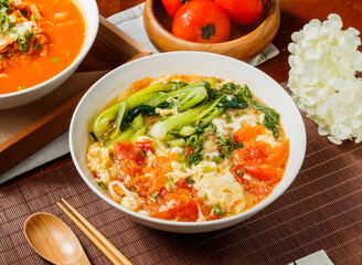 Green vegetable tomato egg noodles soup in bowl isolated on napkin side view on table taiwan food