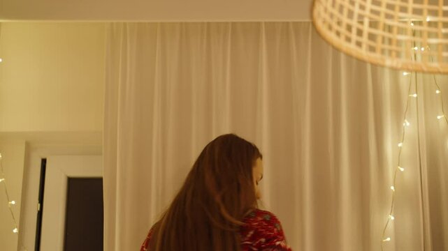 A Woman in a Red Festive Sweater Carefully Adjusting String Lights on a Curtain, Creating a Warm Holiday Ambiance in Her Home.