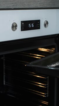 Vertical video. Close-up of woman placing homemade pizza into a modern preheated oven with a digital display, slow motion. Cooking tasty food for family